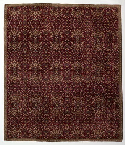 Dense rows of small floral motifs cover a deep red Kashmiri carpet, enclosed by a narrow cream floral border.