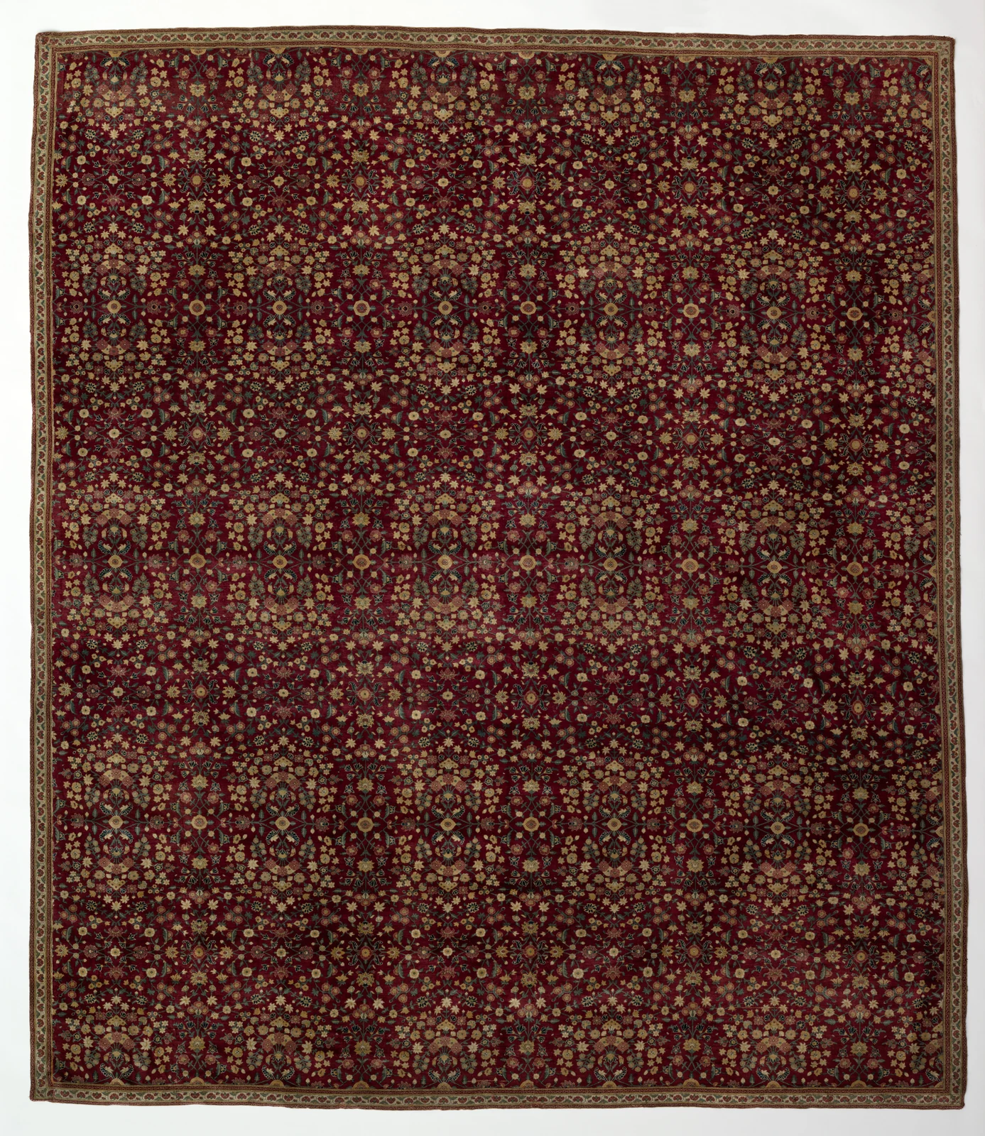 Kashmiri carpet covered in dense rows of small floral motifs on a deep red field with a cream floral border