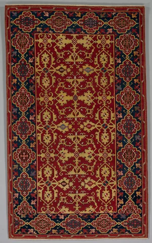 Red Ottoman carpet with a yellow lattice of stylized leaves and a dark blue border containing red-and-gold cartouches.